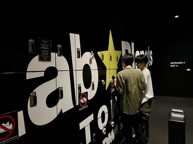 Two people stand in front of branded black storage lockers in the teamLab Planets museum in Tokyo, Japan