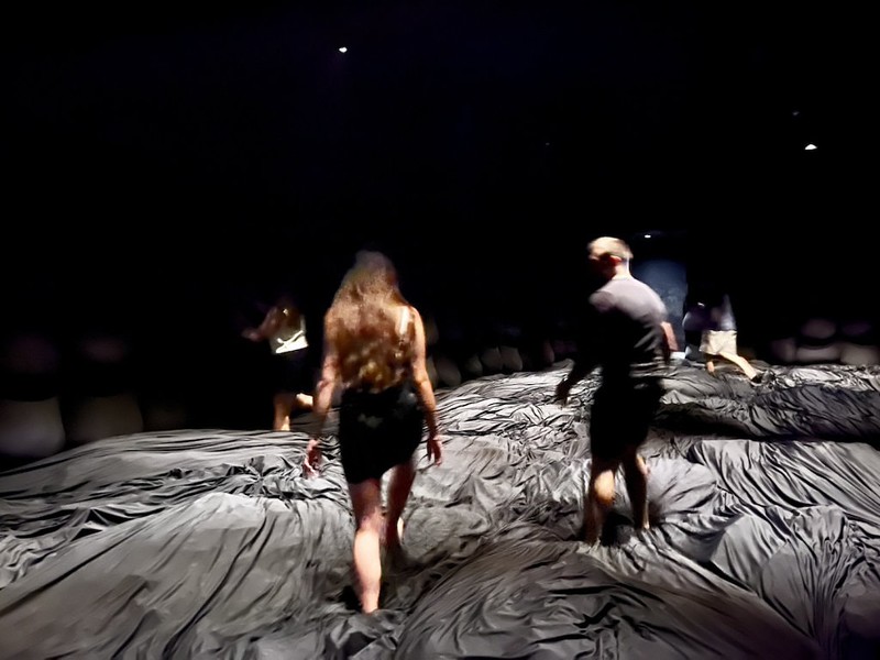 People at the teamLab Planets exhibtion, Tokyo, Japan, walk and bounce around on a springy floor covered in rumpled grey fabric with atmospheric lighting
