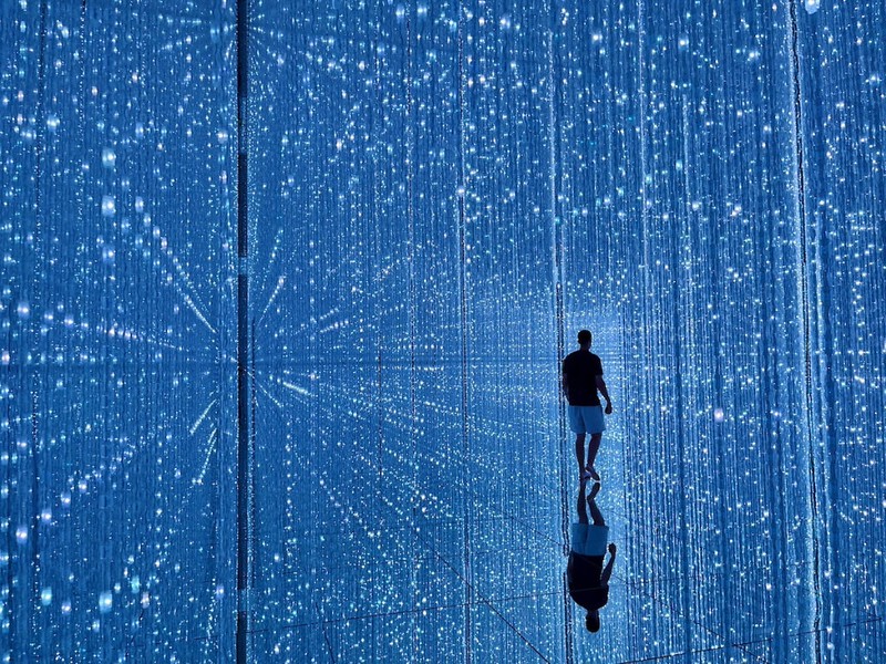 A person stands reflected in the infinity room at the teamLab Planets exhibition, Tokyo, Japan, surrounded by dots of light in all dimensions