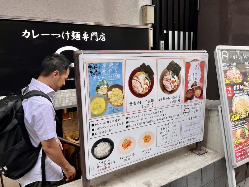 A Japanese tour guide stands in front of the menu board outside a Tokyo ramen restaurant