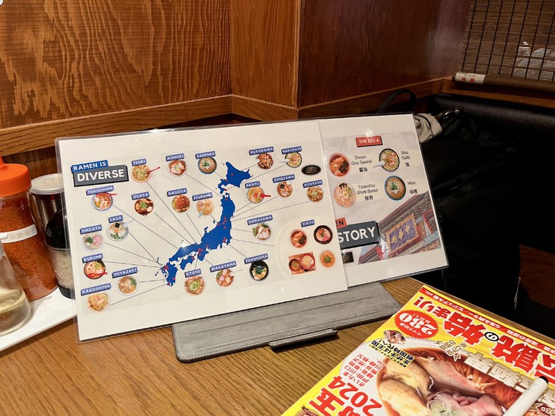 A laminated map of Japan, propped up on a restaurant table, showing different regional variations of ramen dishes