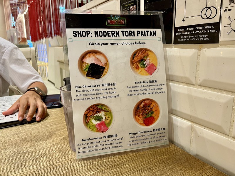A laminated menu of different ramen options to choose on a food tour with pictures of each dish and explanations in English of what they contain