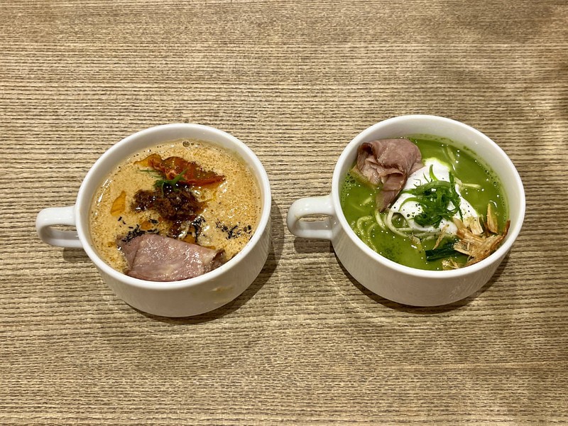 Two cups of ramen on a table in a Tokyo restaurant, with one containing Wagyu tantanmen and the other containing matcha paitan with almond cream