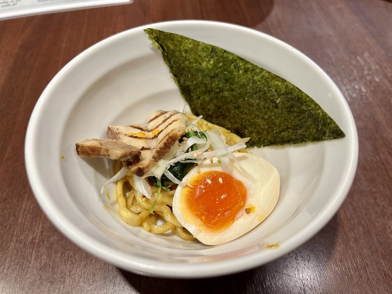 A small bowl of ramen with a layer of shredded vegetables and a gooey boiled egg and no broth