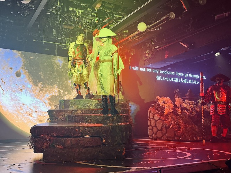 Two performers in Edo-period costumes perform an enka song while a samurai stands guard to the right of the stage at Samurai Restaurant Time