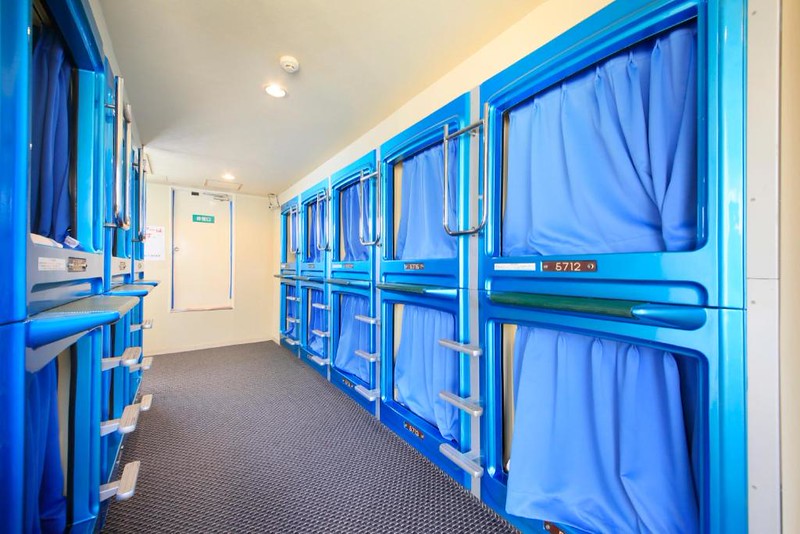 Small corridor with double-decker sleeping capsules with blue, closed curtains in the Ueno Station Hostel Oriental II, Tokyo